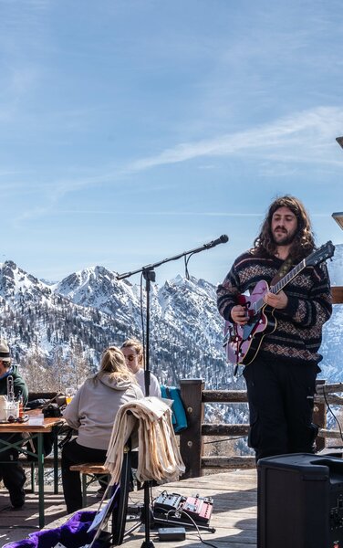 Sänger mit Gitarre spielt mit den verschneiten Dolomiten im Hintergrund. | © Skirama Kronplatz