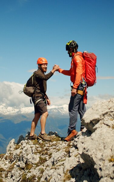 Zwei Bergsteiger am Gipfel angekommen und geben sich die Hand. | © RAW Media