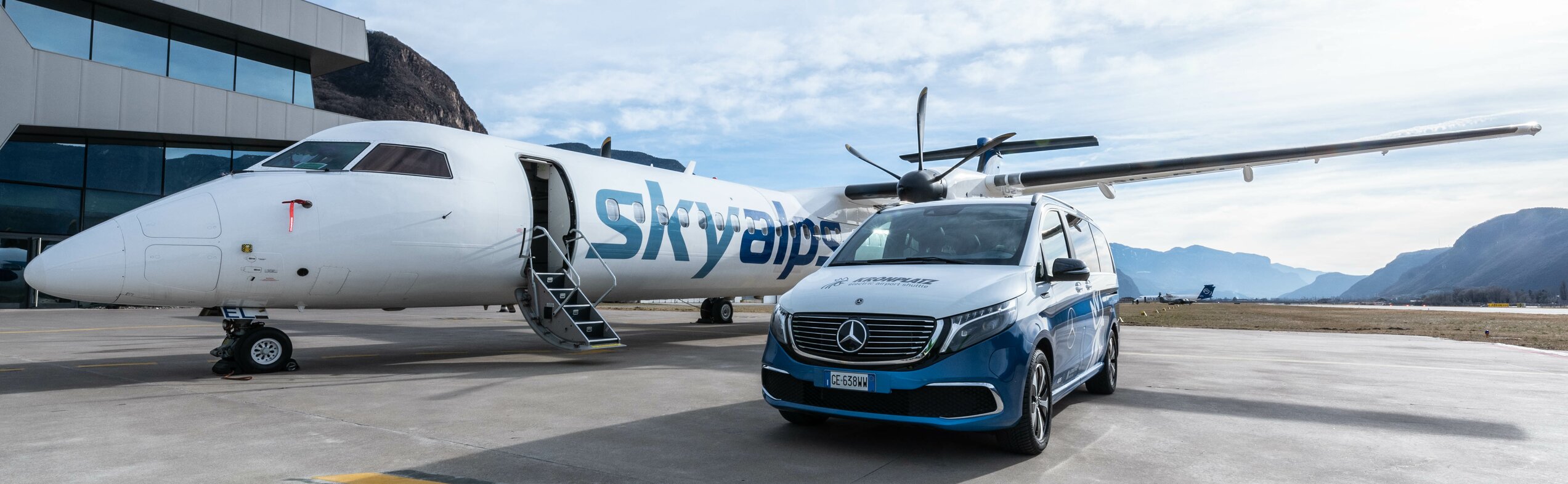 Der Kronplatz Airport Shuttle Bus und ein Skyalps Flugzeug auf dem Flughafen in Bozen. | © Skirama Kronplatz