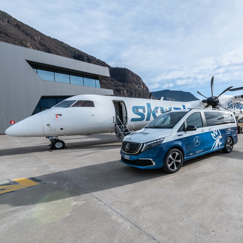 Der Kronplatz Airport Shuttle Bus und ein Skyalps Flugzeug auf dem Flughafen in Bozen. | © Skirama Kronplatz
