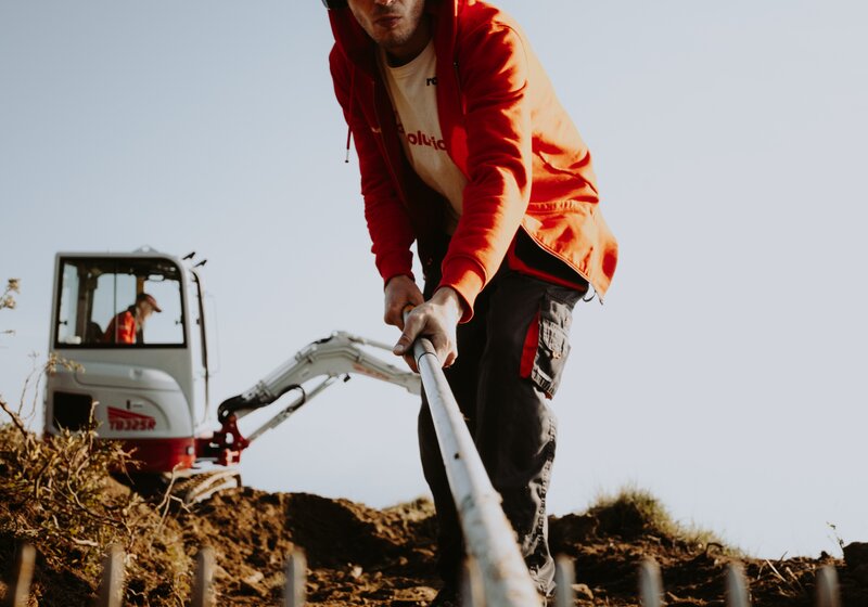 Eine Person mit Schutzbrille und roter Jacke schiebt ein Arbeitsgerät über frischen Boden. | © Daniel Niederkofler