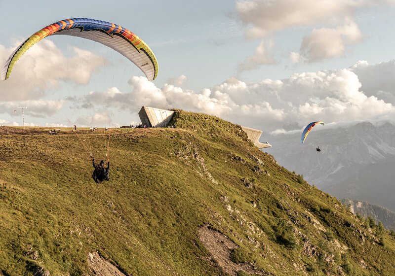 Zwei Paragleiter fliegen um das MMM Corones bei Sonnenuntergang. | © Skirama Kronplatz
