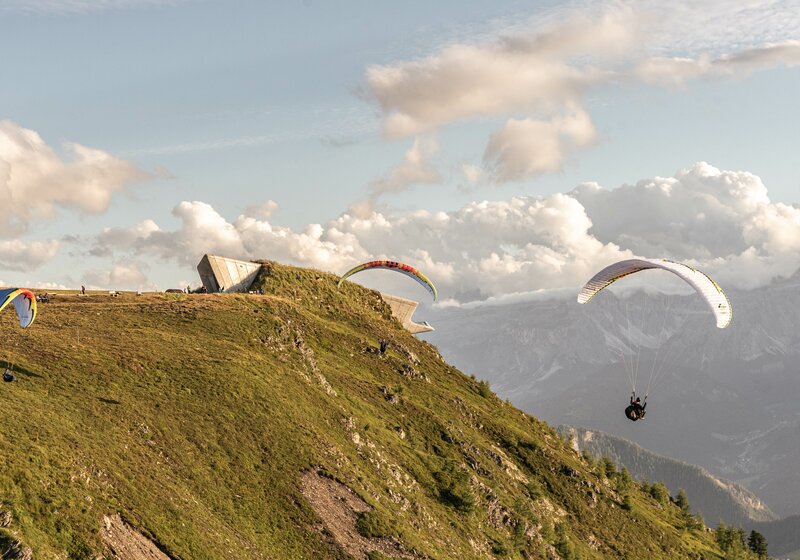 Zwei Paragleiter fliegen um das MMM Corones bei Sonnenuntergang. | © Skirama Kronplatz