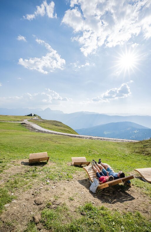 Ein Mann und eine Frau sitzen auf der Liege, genießen die Sonne und schauen auf das MMM Corones und die umliegenden Berge. | © Harald Wisthaler