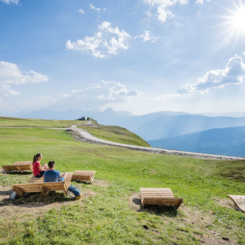 Ein Mann und eine Frau sitzen auf der Liege, genießen die Sonne und schauen auf das MMM Corones und die umliegenden Berge. | © Harald Wisthaler