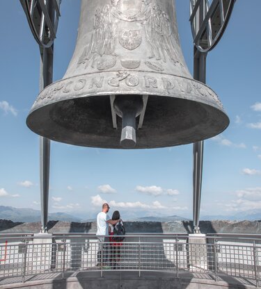Ein Paar schaut sich das Bergpanorama von der Concordia Glocke aus an. | © Skirama Kronplatz