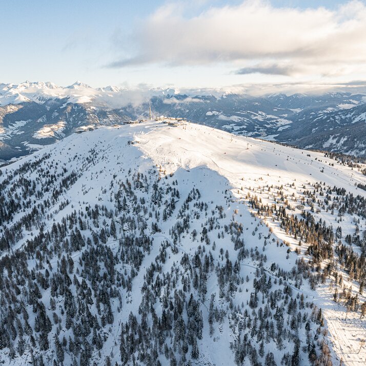 Weitwinkelaufnahme eines verschneiten Berghangs mit bewaldeten Flanken und Sicht auf die umliegenden Alpen. | © Harald Wisthaler