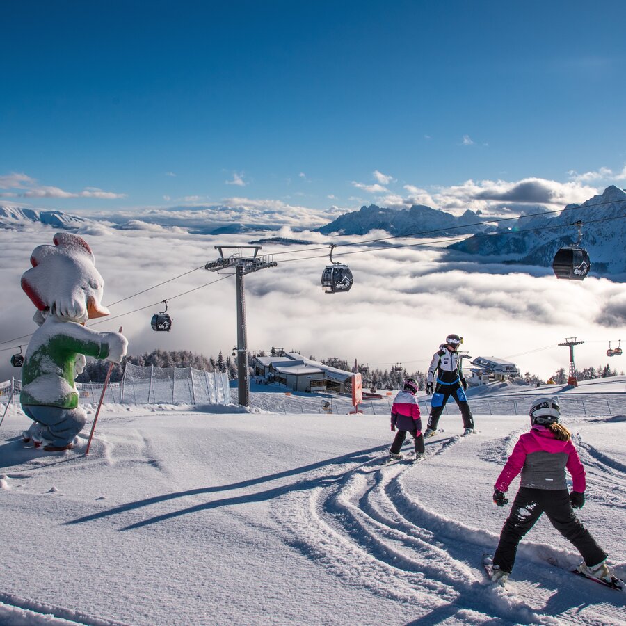 Kinder fahren mit dem Skilehrer im Kids Safety Park bei blauem Himmel. | © Skirama Kronplatz